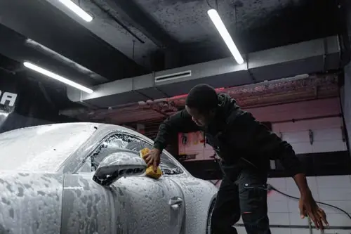 Detailer hand washing the side of a foam-covered vehicle
