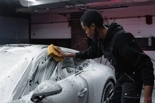 Detailer washing the roof of a foam-covered vehicle